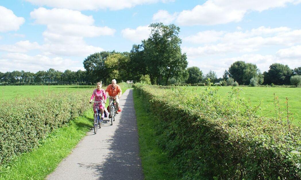 7 leukste fietsroutes om Nederland te ontdekken / Foto: "Twee fietsers op vrijliggend fietspad in natuurgebied Rhijnauwen met aan beide zijden een haag" door CROW-Fietsberaad